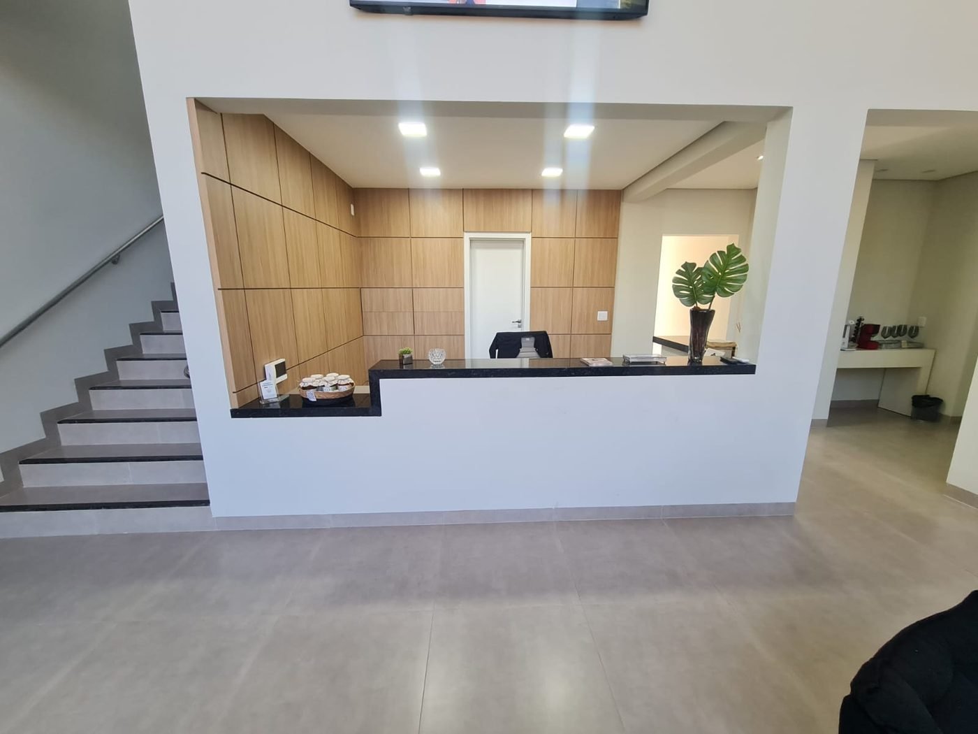 Balcão de recepção em madeira clara e granito preto, ao lado da escada